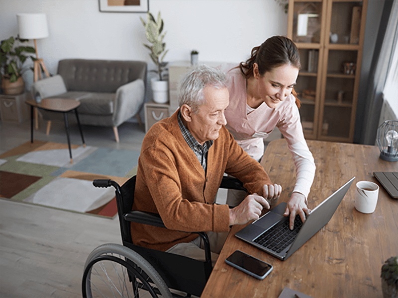 Nurse assisting elderly patient with his laptop